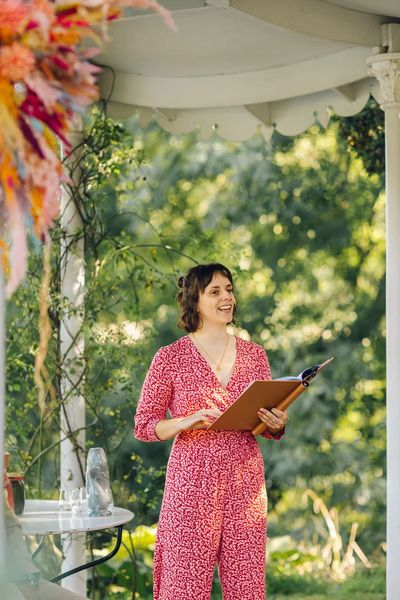 Hannah is reading aloud from her ceremony folder. She is smiling and wearing a pink jumpsuit.